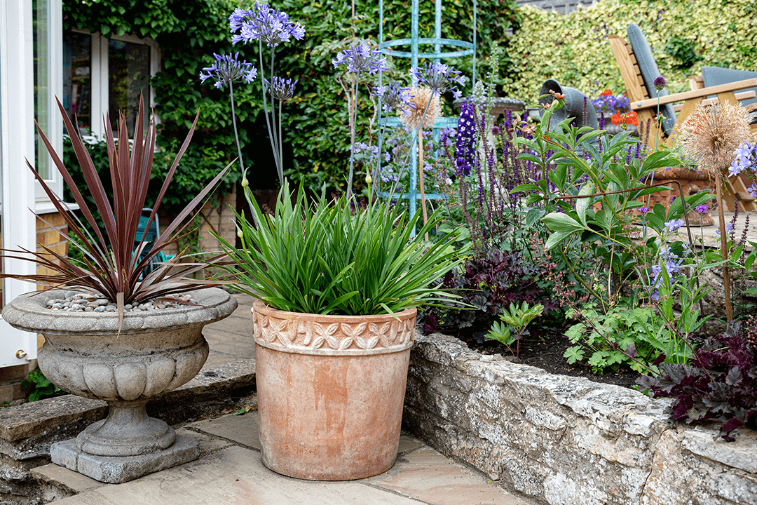 A close up of some stylish pots and a natural stone border with a variety of plants on display.