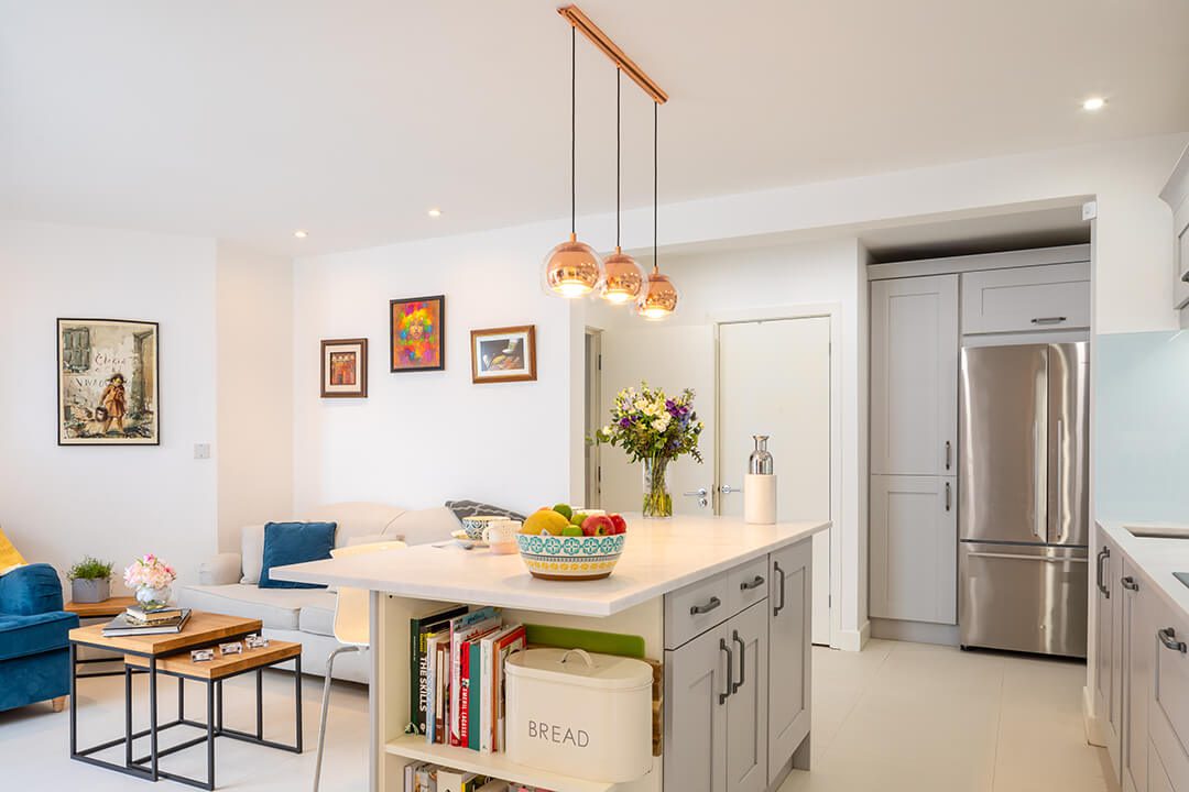A view across the open plan living and kitchen area in a mews house property featuring a set of copper light shades over the top of the kitchen island.
