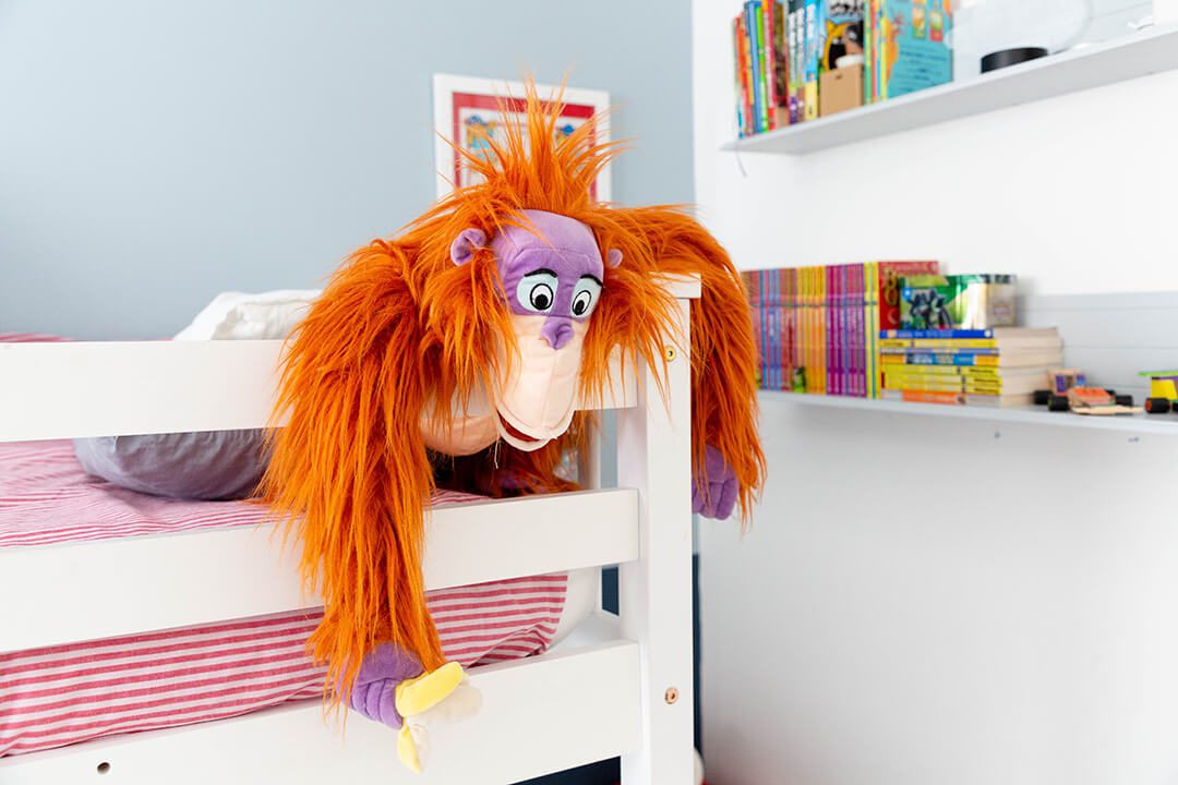 Close up of a cuddly toy orange orangutan with a banana leaning over the railings of a bunk bed.