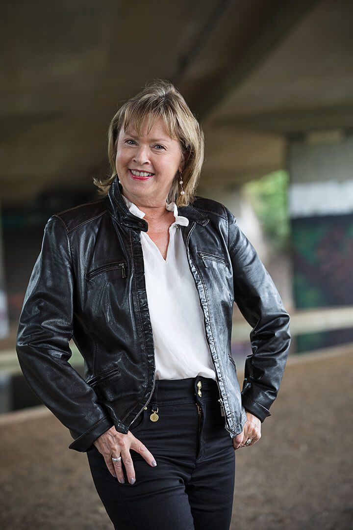 A relaxed corporate portrait of a mature woman under a motorway flyover with a canal in the background