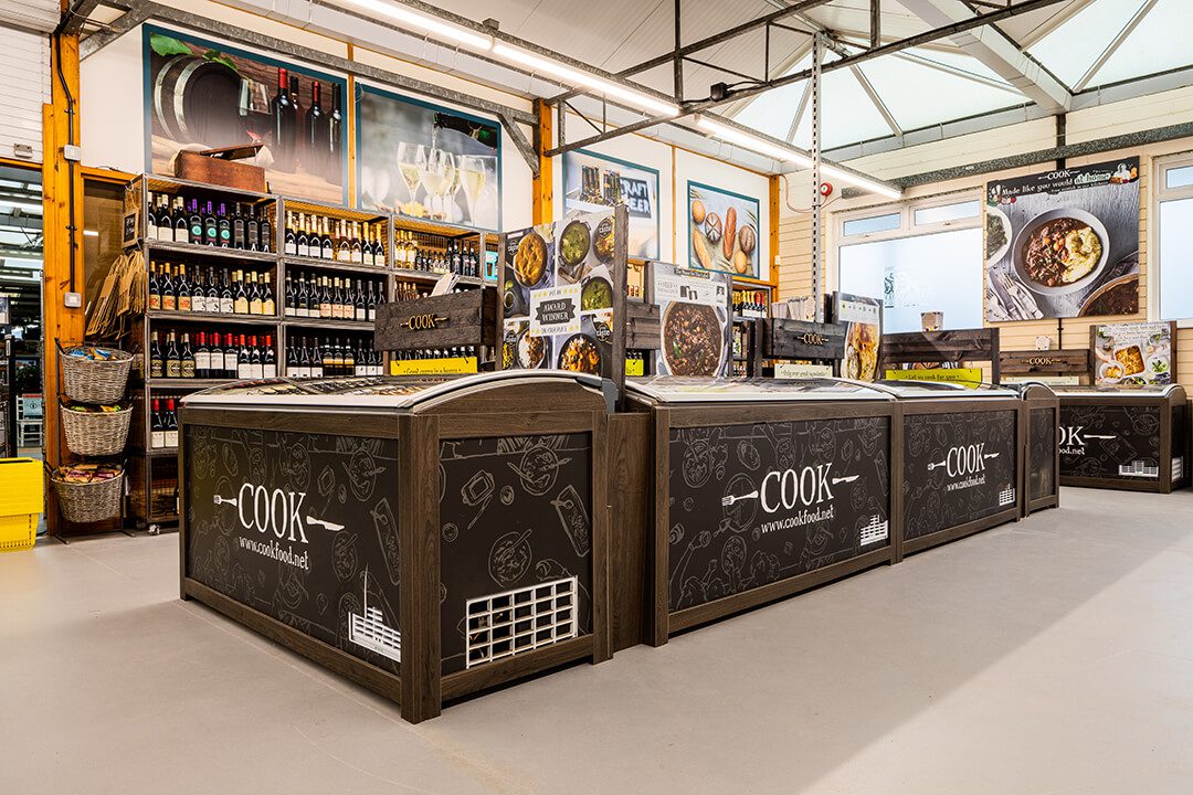 An overview of the corner of a farm shop showing the display freezers for the 'Cook' range of frozen meals