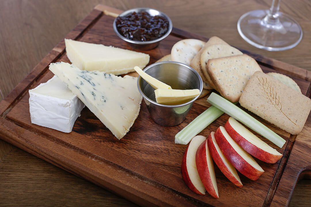 Overhead view of a cheeseboard with three types of cheese, biscuits and fruit in a pub