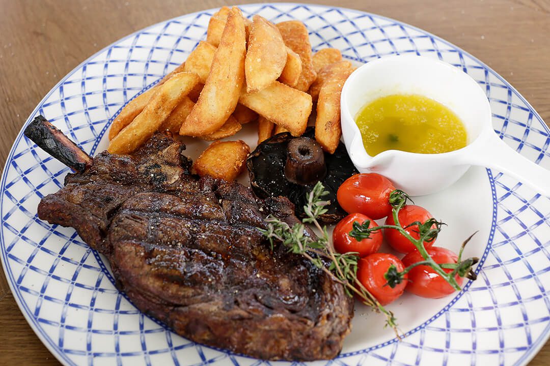A bright image showing a tasty steak served with chunky chips and tomatoes on the vine.