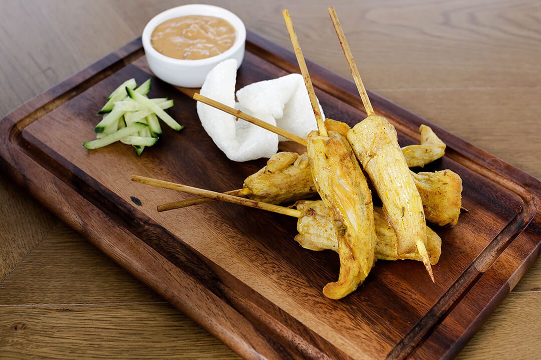 A set of chicken satay on skewers served with a dip on a wooden board