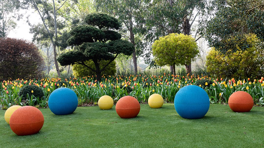 A view across part of the new childrens garden at Kew. There are bright coloured balls on the lawn in the foreground with flower beds behind