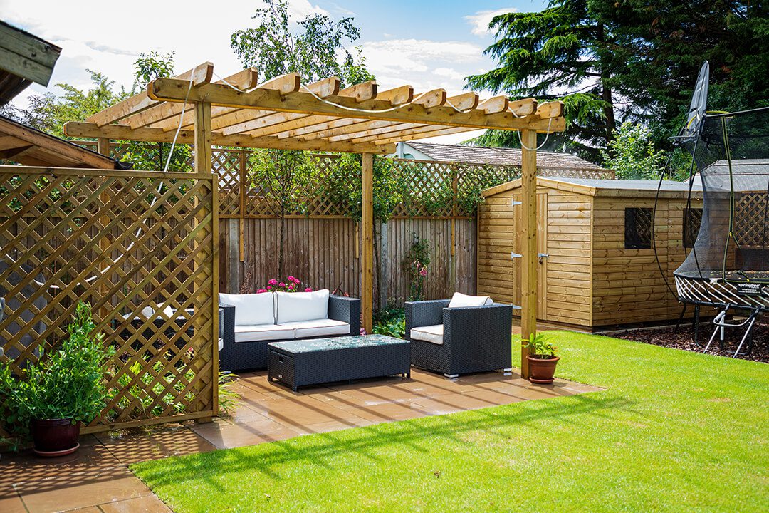 A bright view of a garden design featuring a wooden pergola and screening for a family area for entertaining