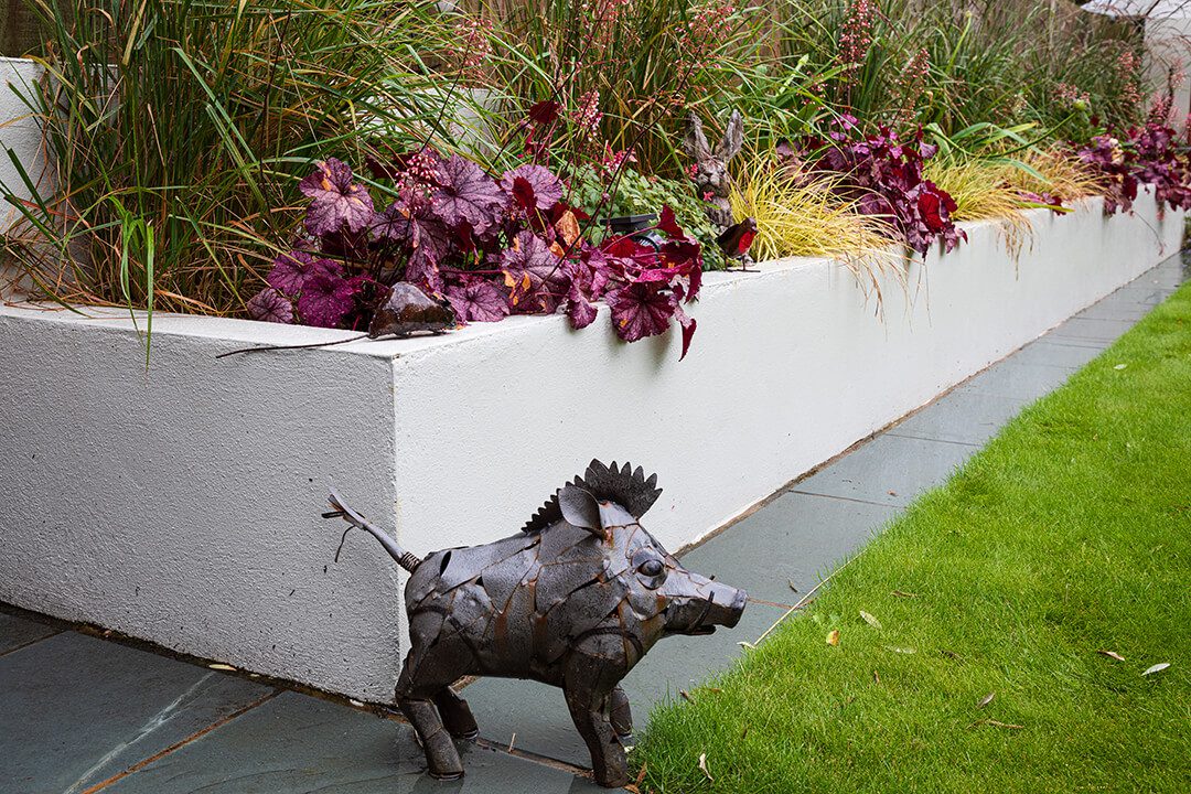 Detail shot from a garden design project featuring concrete planters filled with soft grasses. There is a metallic sculpture of a warthog in the foreground.