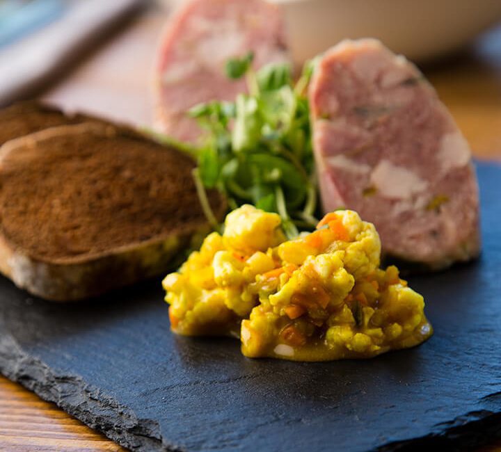side on view of a slate containing fresh pate, toast and a bright yellow salsa.